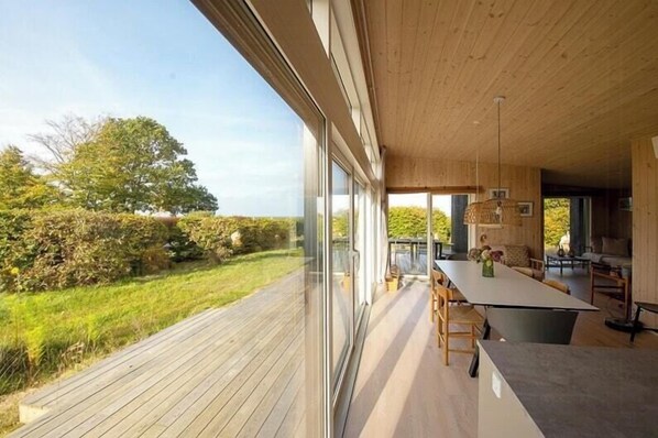 A modern interior with a large sliding glass door, a wooden deck, and a dining area with a table and chairs. - Beautiful setting by the sea with light and sky (Grenå)