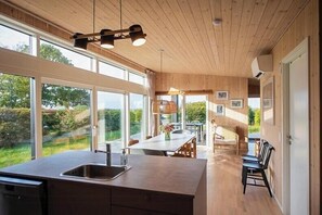 A modern kitchen with a large island, a dining area with a table and chairs, and a view of the outdoors. - Beautiful setting by the sea with light and sky (Grenå)