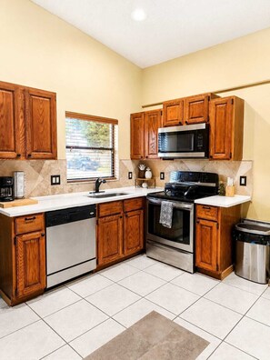 A kitchen with wooden cabinets, a dishwasher, a stove, and a trash can. - Casa de Halo (Orlando)