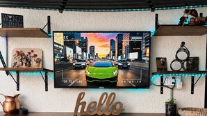 Een bar met een televisiescherm waarop een stadsgezicht te zien is, een bord met de tekst 'hello' en een bar en krukken.