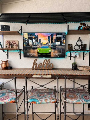 Eine Bar mit Fernsehbild einer Stadtansicht, einem 'hello'-Schild und einer Bar mit Hockstühlen.