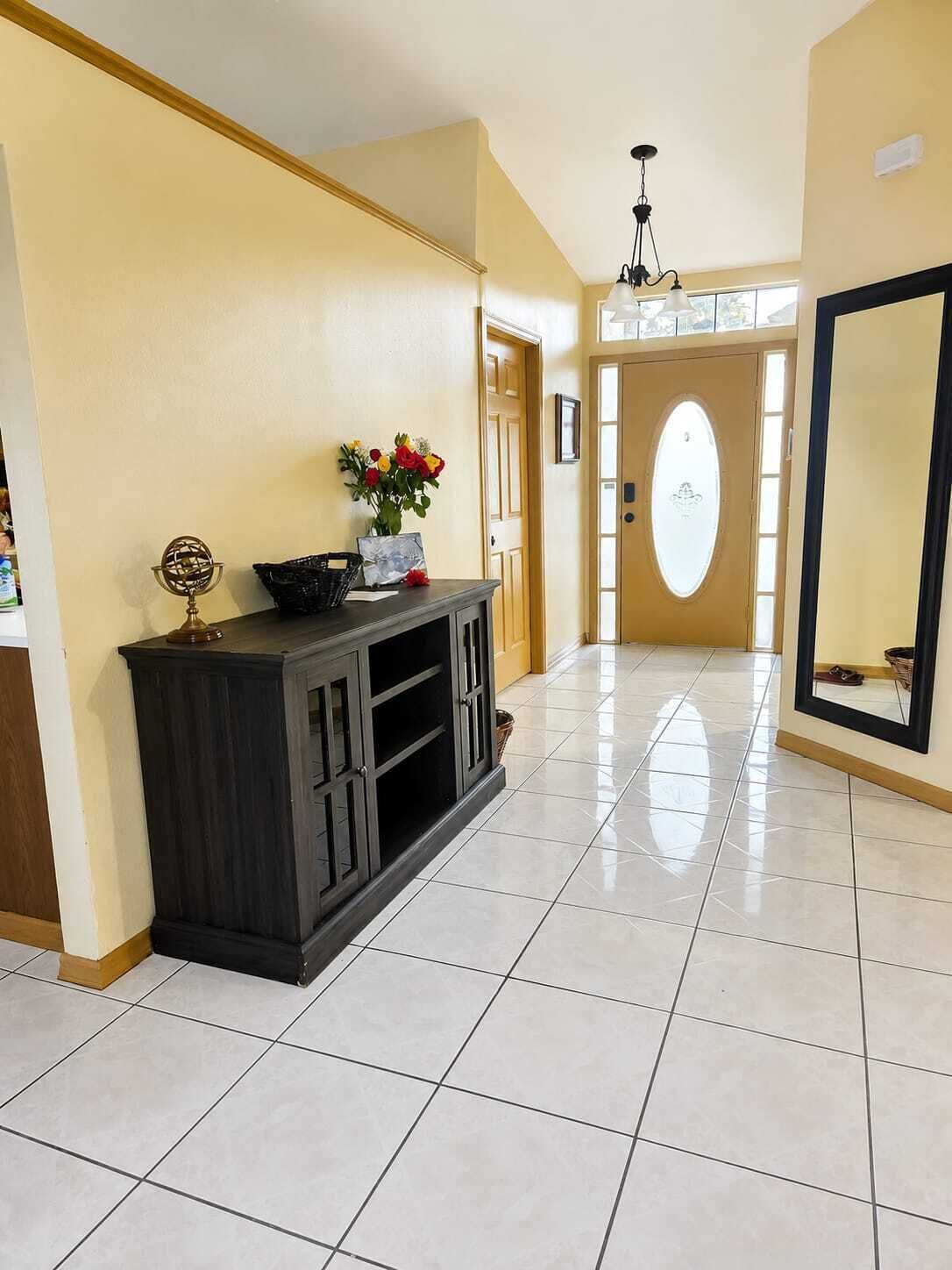 Een gang met een donker houten console tafel, een vaas met bloemen en een grote spiegel aan de muur.