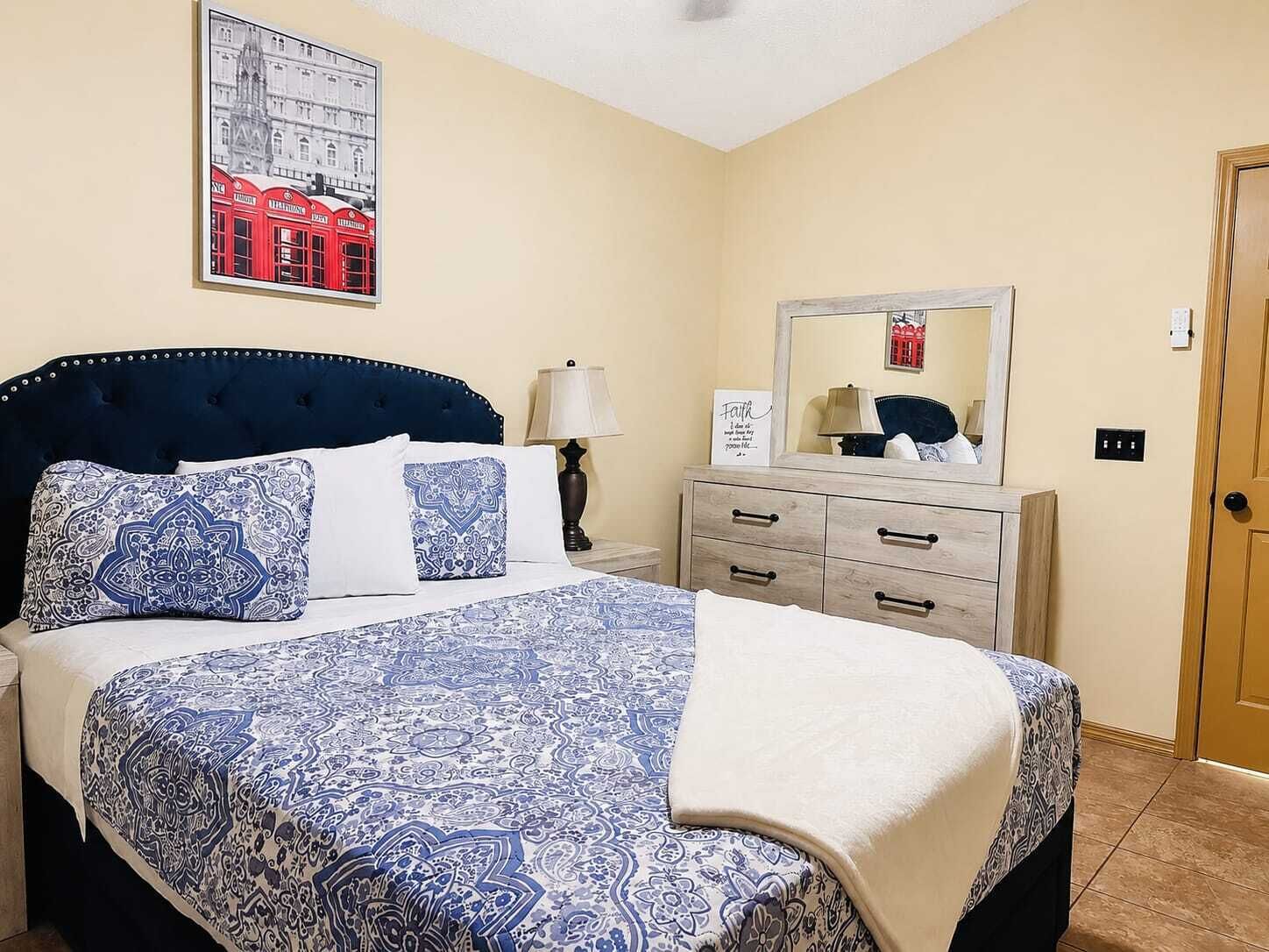 A bedroom with a bed, a nightstand, a dresser, a mirror, and a wall-mounted picture.