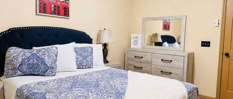 A bedroom with a bed, a nightstand, a dresser, a mirror, and a wall-mounted picture.