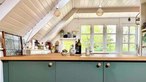 A kitchen with a wooden countertop, green cabinets, and a window with a view of greenery. - Colorful summerhouse close to the sea (Maribo)