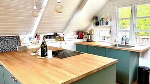 A kitchen with a wooden countertop, a built-in stove, and a window with a view of greenery. - Colorful summerhouse close to the sea (Maribo)
