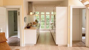 A modern kitchen with white cabinetry, pendant lighting, and a view through large windows. - Red stone house by Dueodde Beach (Nexø)