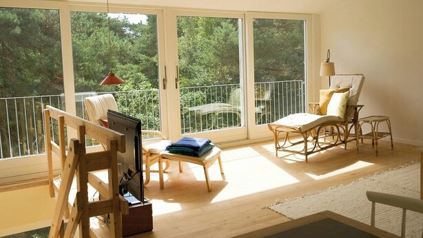 A room with large sliding glass doors, a wooden easel, a chair, and a table. - Red stone house by Dueodde Beach (Nexø)