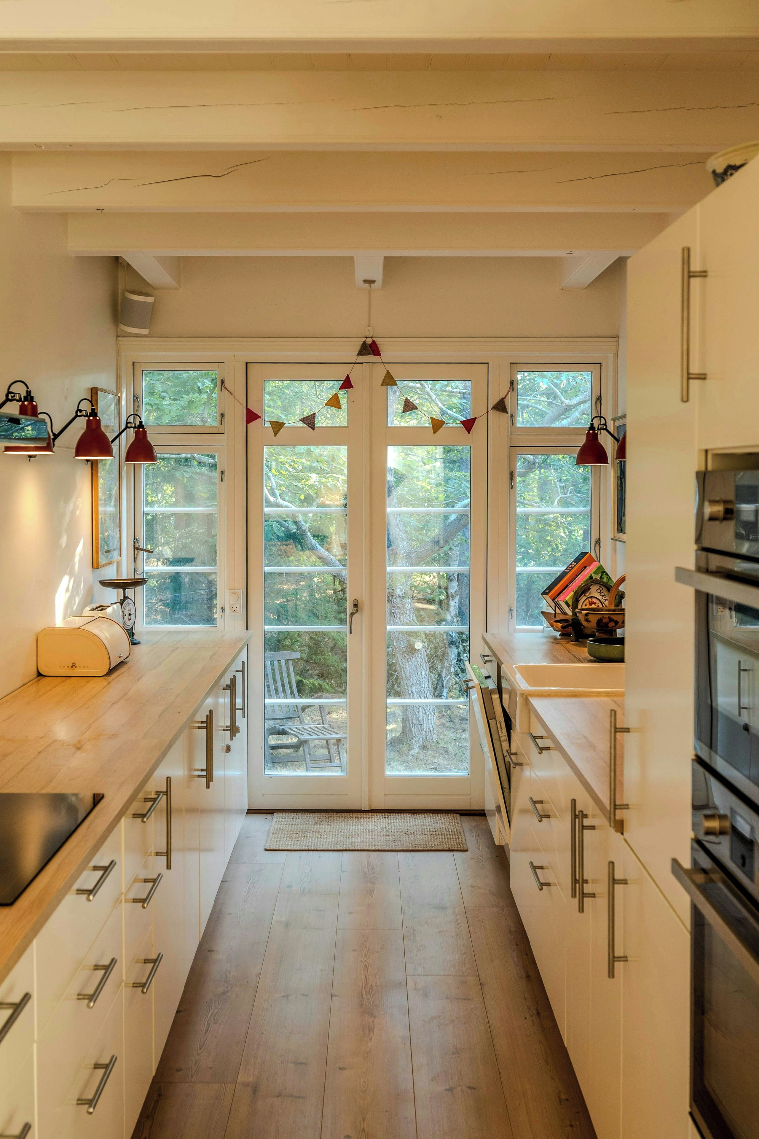 Cozinha moderna com armários brancos, bancada de madeira e vista através das portas de vidro.