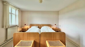 A double bed with two bedside tables, each with a lamp, in a room with a window and a radiator.