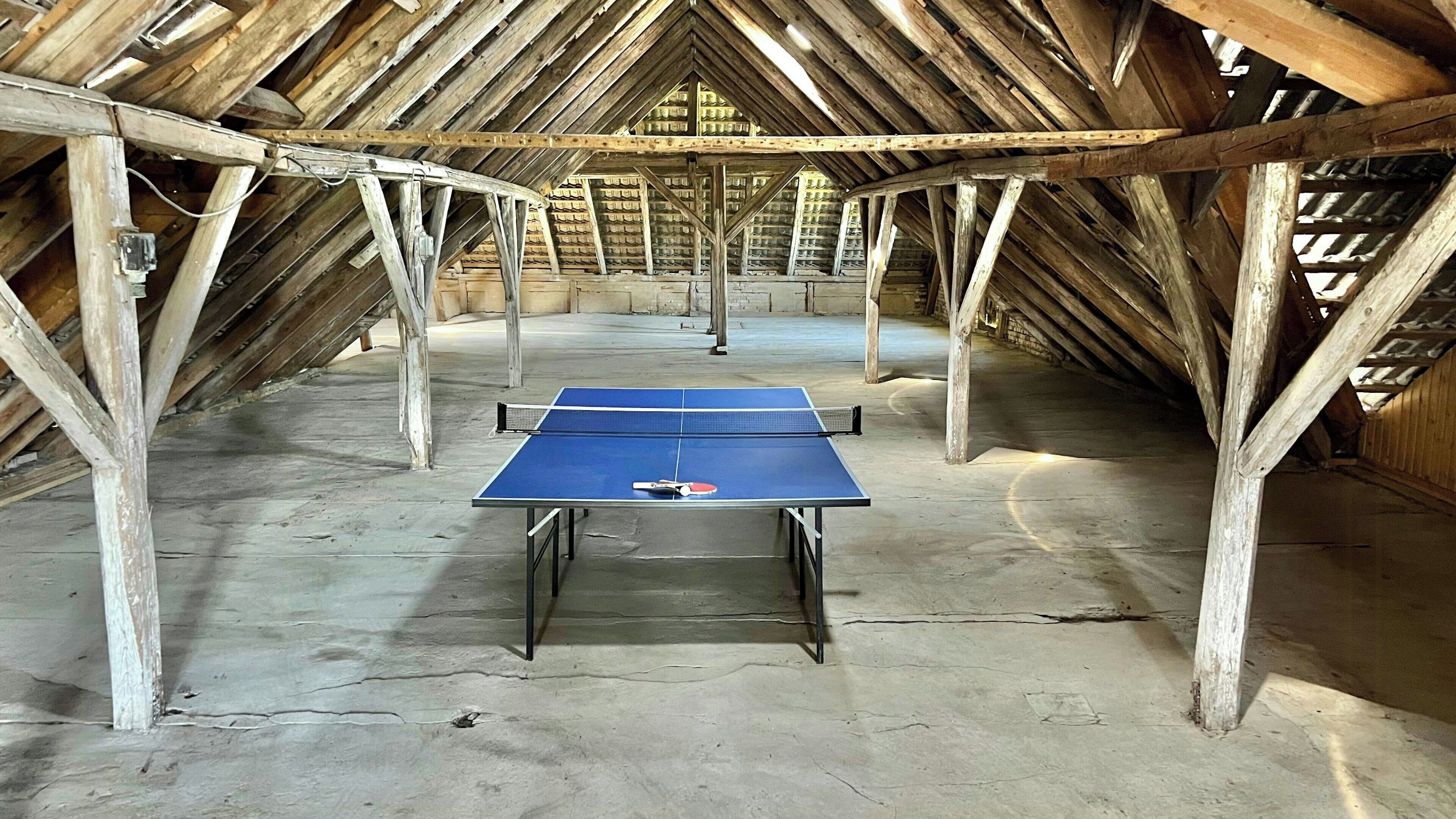 An attic room with a ping pong table, wooden beams, and a sloped ceiling.