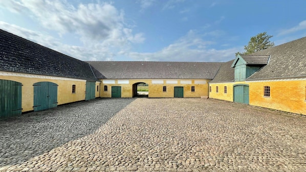 A courtyard with cobblestone flooring, yellow buildings, green doors, and a clear sky.