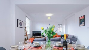Un comedor con una mesa preparada para seis personas, un florero con flores y un televisor al fondo.