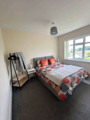 A bedroom with a bed, a bedside table, a hanging light fixture, a window with a view, and a coat rack. - Comfortable 3BR Sleeps 7 | Contractor Stays (Ewloe)
