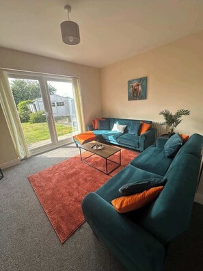 A living room with a sofa, a coffee table, and a view through a glass door. - Comfortable 3BR Sleeps 7 | Contractor Stays (Ewloe)