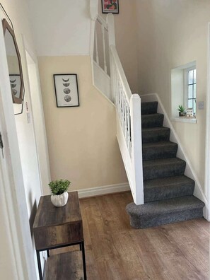 A staircase with a white handrail and dark carpeted steps, a small table with a plant, and a framed picture of moons on the wall. - Comfortable 3BR Sleeps 7 | Contractor Stays (Ewloe)