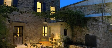 A stone building with a courtyard, outdoor seating, and a staircase leading to an upper level.