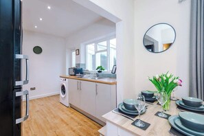 A modern kitchen with a washing machine, a dining area with a table set for four, and a mirror on the wall. - Comfortable 3BR Sleeps 6 | Contractor Stays (Flintshire)