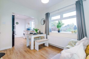A modern kitchen with a dining area, a large window with curtains, and a view of greenery outside. - Comfortable 3BR Sleeps 6 | Contractor Stays (Flintshire)