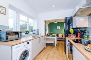 A modern kitchen with a washing machine, a microwave, and a dining area with a table and chairs. - Comfortable 3BR Sleeps 6 | Contractor Stays (Flintshire)