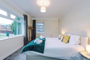 A hotel room with a bed, a window, a bedside table, and a lamp. - Comfortable 3BR Sleeps 6 | Contractor Stays (Flintshire)