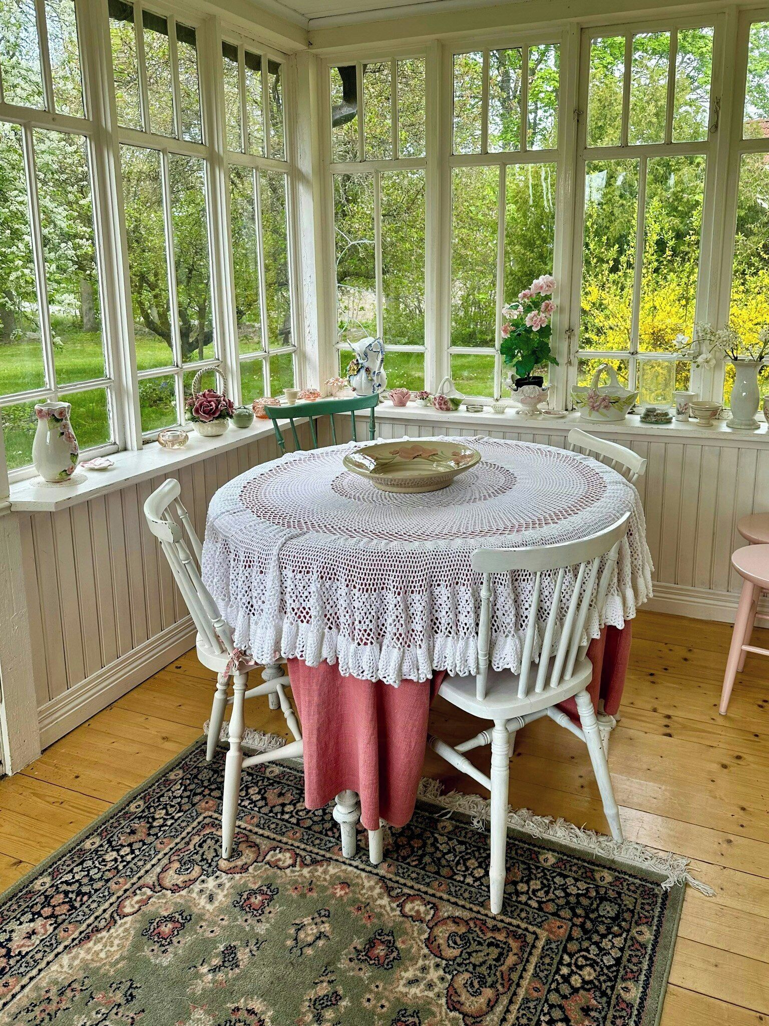 Une véranda avec une table ronde, des chaises et une vue sur la verdure environnante.