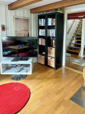 Un salon avec un téléviseur à écran plat, une bibliothèque, un tapis rouge et un escalier en bois.
