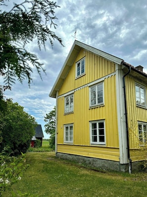 Une maison jaune à deux étages, avec un toit en pente, de nombreuses fenêtres et une cheminée.