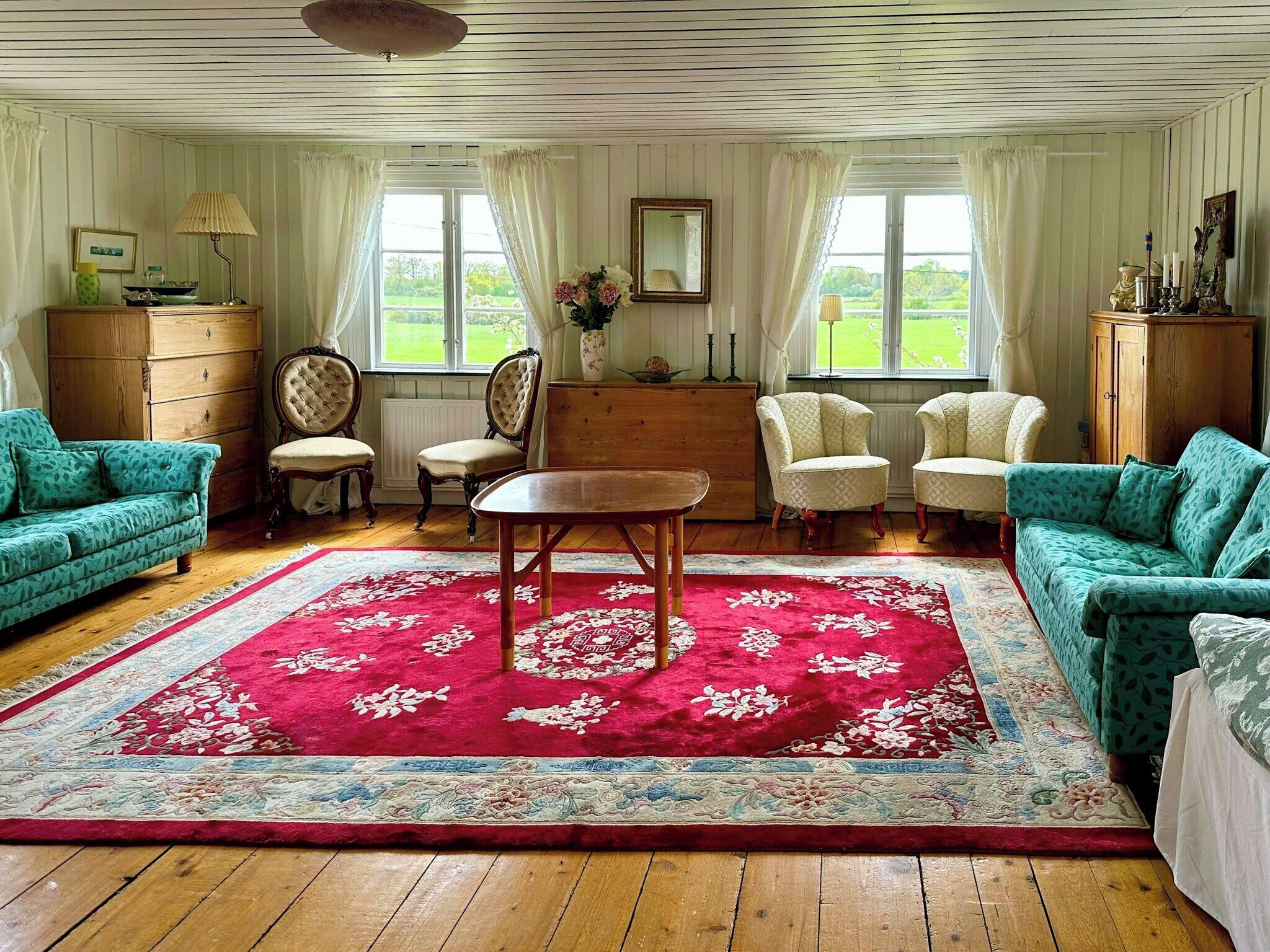 Una habitación con dos sofás verdes, una mesa de madera y un tapete rojo con estampado floral.