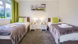 Ein Doppelzimmer mit zwei Betten, Nachttischen, Lampen und einem Fenster mit Vorhängen.
