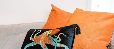A bed with a grey blanket, an orange pillow, and a black pillow with an octopus design.