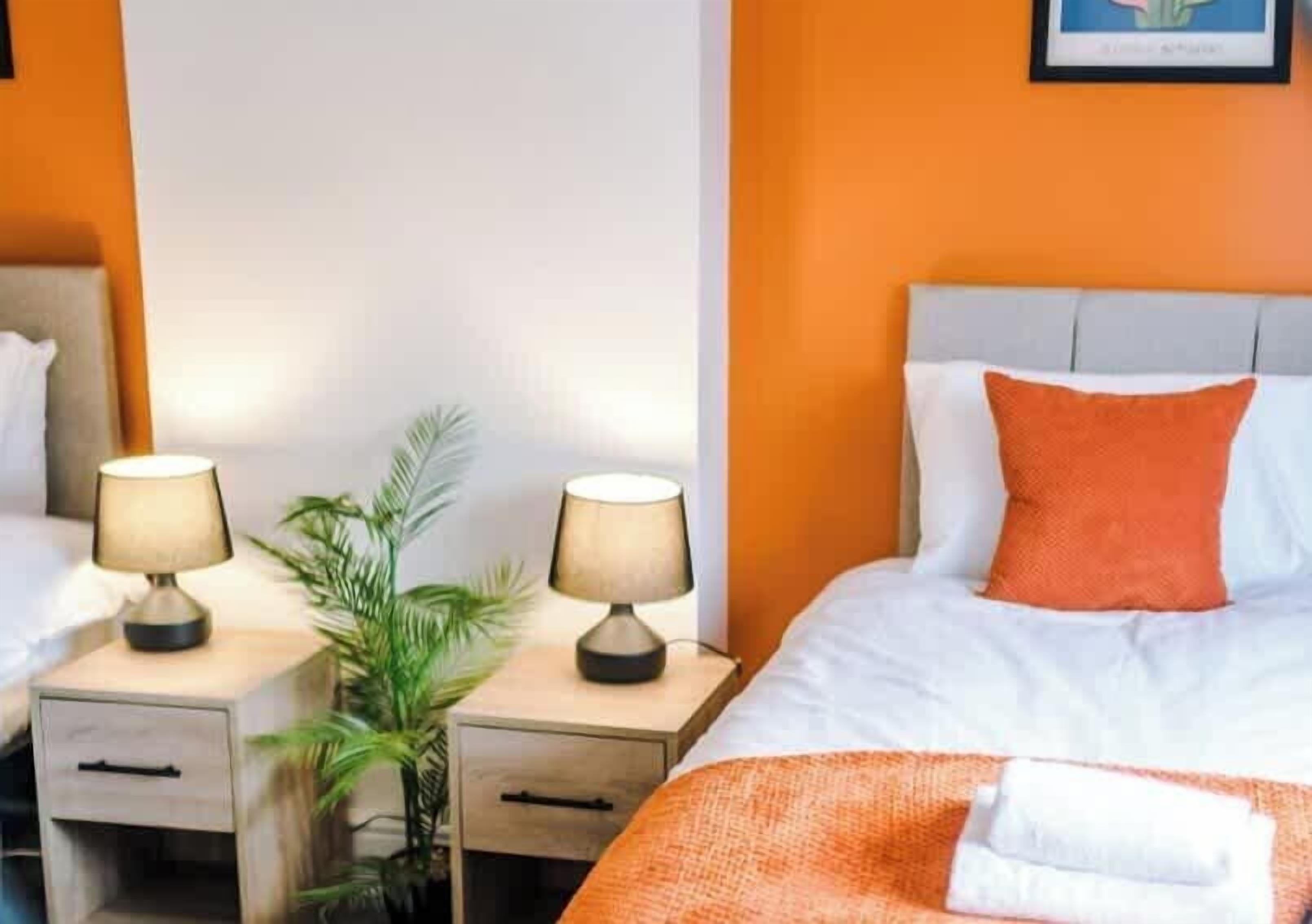 A hotel room with a bed, two bedside tables with lamps, a potted plant, and a framed picture on the wall.