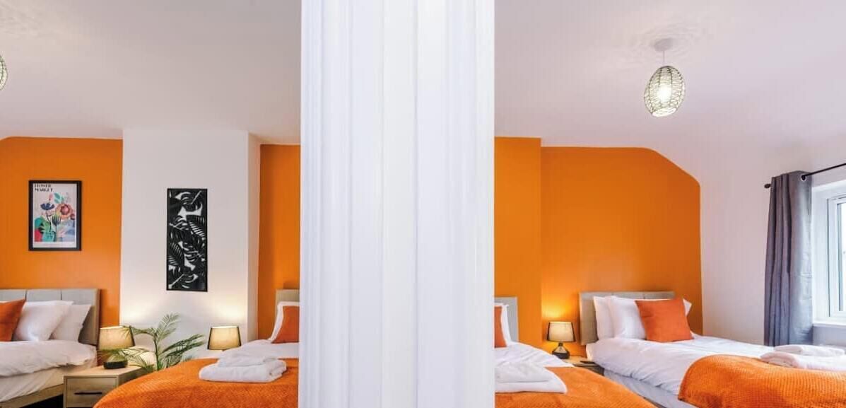 Een hotelkamer met twee bedden, oranje wanden, witte gordijnen en kunstwerken aan de muur.