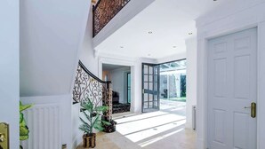 A spacious hallway with a white door, a staircase with a decorative railing, and a view of the outdoors. - Hawarden Exec 5BR | 7 Beds | Contractor Stays (Hawarden)