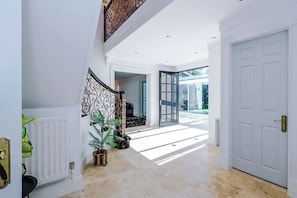 A spacious hallway with a white door, a staircase with a decorative railing, and a view of the outdoors. - Hawarden Exec 5BR | 7 Beds | Contractor Stays (Hawarden)