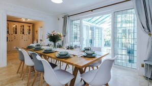 A dining room with a long wooden table set for six, white chairs, and a large window with a view. - Hawarden Exec 5BR | 7 Beds | Contractor Stays (Hawarden)