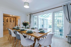 A dining room with a long wooden table set for six, white chairs, and a large window with a view. - Hawarden Exec 5BR | 7 Beds | Contractor Stays (Hawarden)