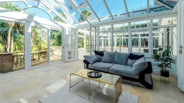A conservatory with a glass ceiling, a grey sofa, and a coffee table. - Hawarden Exec 5BR | 7 Beds | Contractor Stays (Hawarden)
