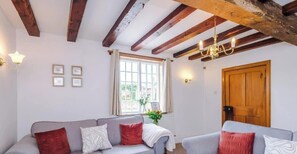 Et hyggeligt rum med trælofter, et vindue med gardiner, en trädør og en sofa med puder.