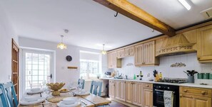 Een keuken met houten keukenkastjes, een eettafel gedekt voor vier personen, en een fornuis.