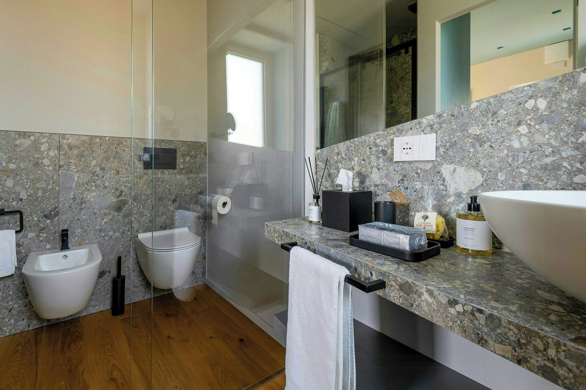 Een moderne badkamer met een marmeren aanrechtblad, een groot wastafel, een bidet en een douche met glazen wanden.