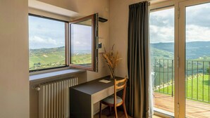 Una habitación moderna con escritorio, silla y vistas a un paisaje verde a través de amplios ventanales.