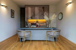 A modern reception desk with a blue countertop, two grey upholstered chairs with gold legs, a decorative vase with pampas grass, and a wall-mounted mirror. - Design farmhouse with jacuzzi among vineyards (Alba)