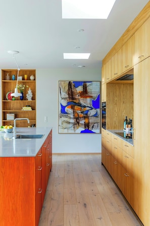 Eine moderne Küche mit Holzausstattung, einer zentralen Kochinsel und einem großen abstrakten Gemälde an der Wand.