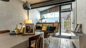 Ett modernt kök med en matplats, en soffa med kuddar, en hängande lampa och utsikt genom en skjutdörr.