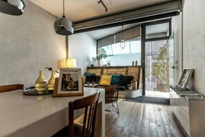 Une cuisine moderne avec un coin repas, un canapé avec des coussins, un luminaire suspendu et une vue à travers une porte coulissante.