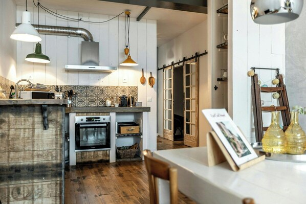 Une cuisine dotée d’un plan de travail en bois, d’un four, d’un luminaire suspendu et d’une porte coulissante donnant sur une autre pièce.