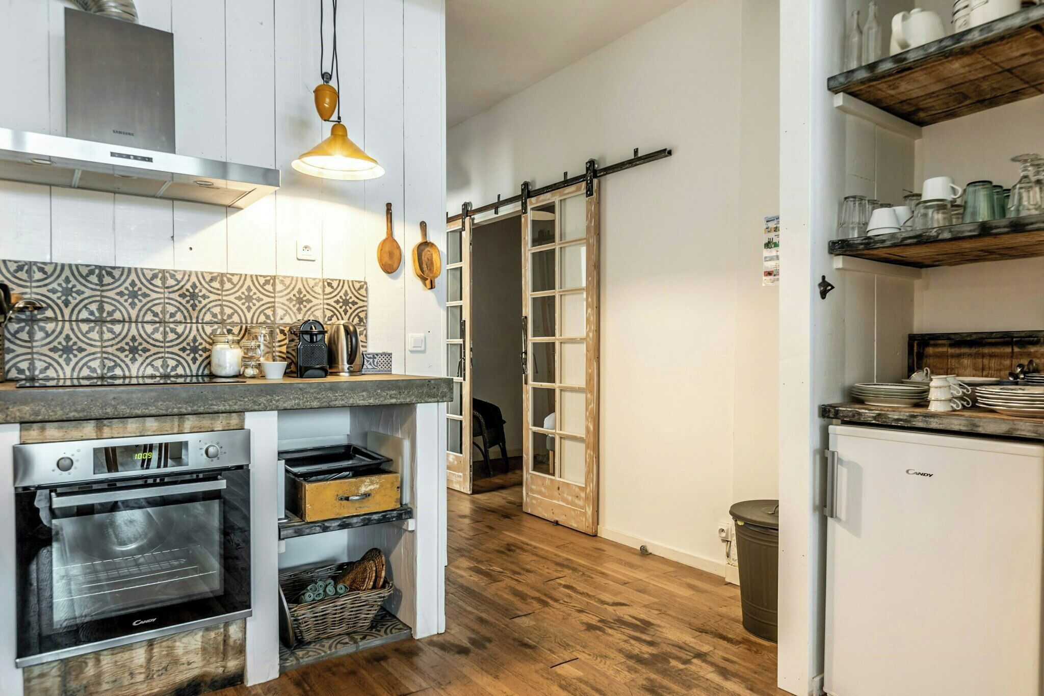 A kitchen with built-in ovens, a sliding door, and wooden shelves.
