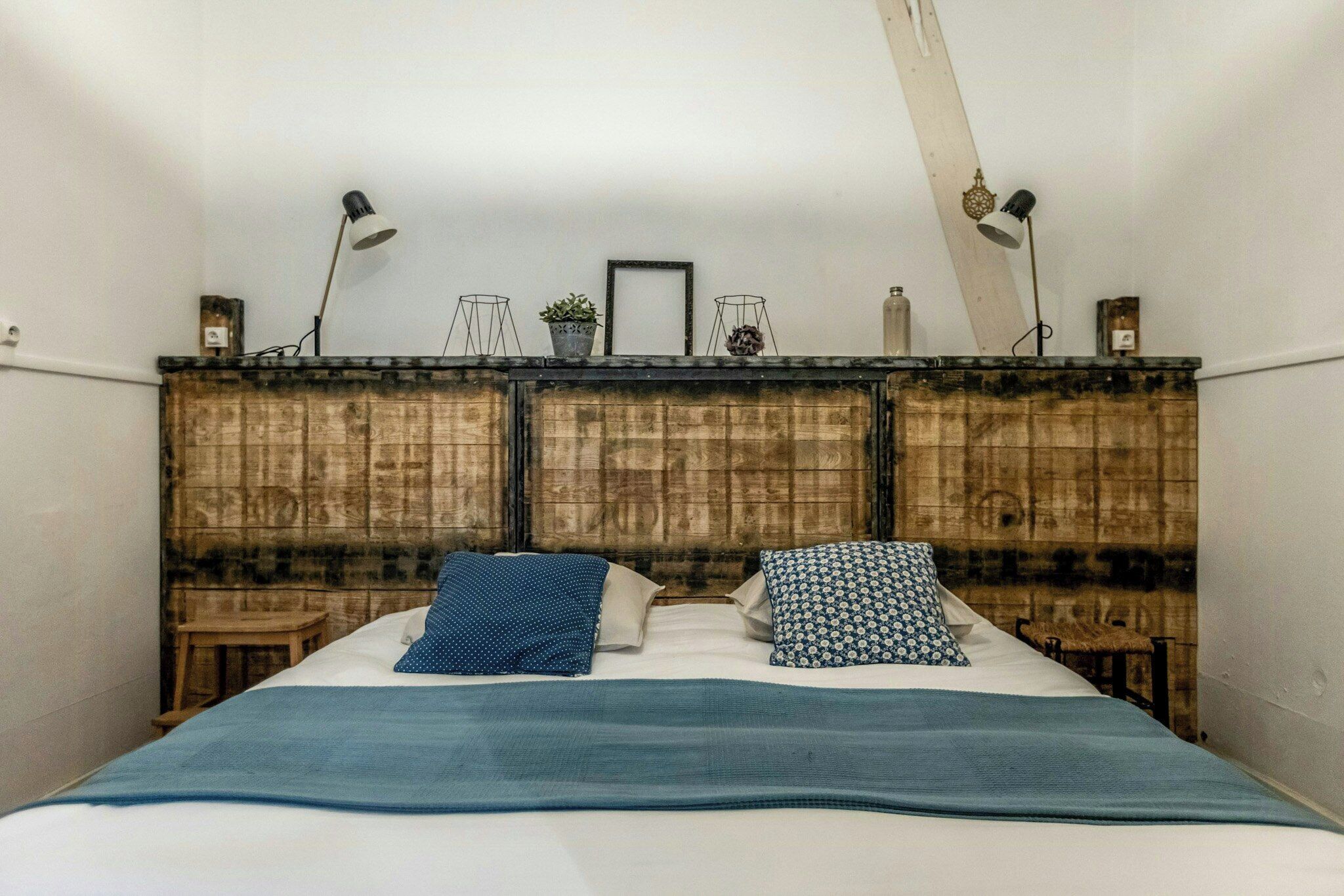 Une chambre à coucher avec une tête de lit en bois, deux tables de chevet, un lit avec une literie bleue et deux lampadaires.