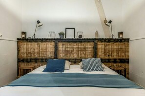 Une chambre à coucher avec une tête de lit en bois, deux tables de chevet, un lit avec une literie bleue et deux lampadaires.